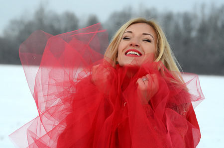 beautiful white blond girl with blue eyes, long hair in the snow in a red dress with a red veil, red lipstickの写真素材