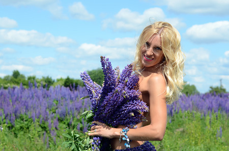 beautiful white blond girl with long hair, blue eyes, with a large bouquet of purple flowers in a field of purple flowers in the summer on a sunny dayの写真素材