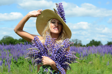 beautiful white blond girl with long hair, blue eyes, with a large bouquet of purple flowers in a field of purple flowers in the summer on a sunny dayの写真素材