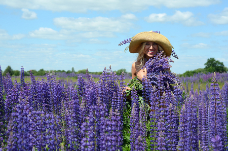beautiful white blond girl with long hair, blue eyes, with a large bouquet of purple flowers in a field of purple flowers in the summer on a sunny dayの写真素材