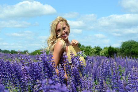 beautiful white blond girl with long hair, blue eyes, with a large bouquet of purple flowers in a field of purple flowers in the summer on a sunny dayの写真素材