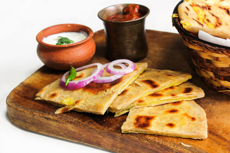 Aloo Paratha served in wooden board with raita and pickle against white background, selective focus