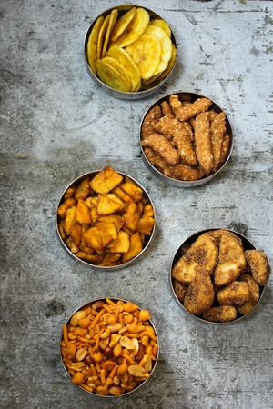 Variety of Indian snacks - Mixture, Tapiyoca , banana chips,Sarkara varatti, Sesame sticks served in metal bowls, top down viewの写真素材