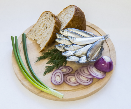 Sprat of spicy salting onion, greens and bread on a wooden platterの写真素材