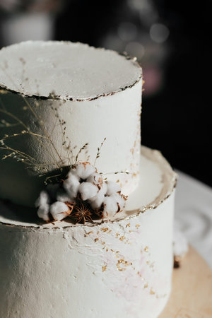 A wedding cake. Milk-colored cake decorated with cotton beads and gold leaf on a dark background