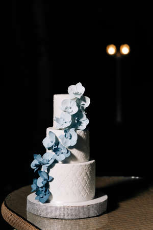 A wedding cake. sweets. Wedding cake on a black background three floors with white mastic decorated with blue and blue orchids from mastic on the tablein wedding dayの写真素材
