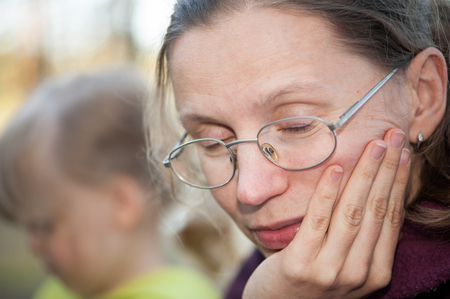 Portrait of a young woman with glasses who is drowsy putting her hand under her head against the background of her daughterの写真素材