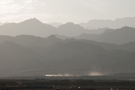 Monochrome landscape of mountain ridge silhouette in a haze at a distance and dusty tail behind the car traveling through the desert in Sinai Egypt.の写真素材