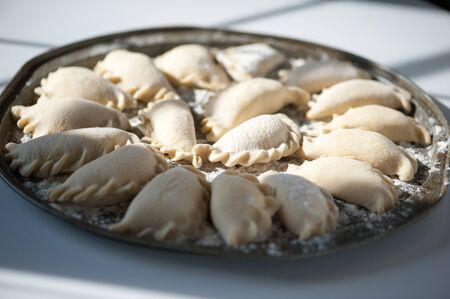A large round dish on a white background with shadows from a window sash with classic raw dumplings sprinkled with flour.の写真素材