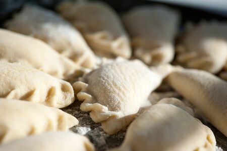 A large round dish on a white  with shadows from a window sash with classic raw dumplings sprinkled with flour.の写真素材