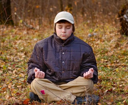 sitting boy meditate in autumn forestの写真素材