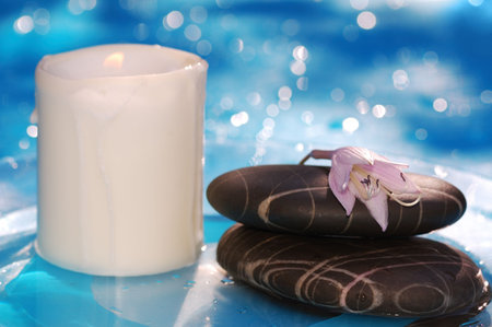 spa stones with candle against blue shining water backgroundの写真素材