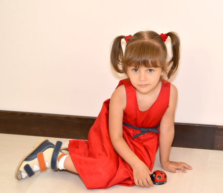 The little girl in a red dress sits on a floor with a toyの写真素材