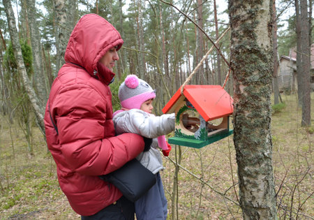 The young man with the daughter put grains in a birds feeder. The family