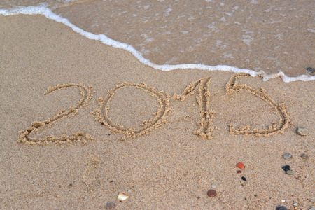 The running wave washes away an inscription "2015" on a sandy beachの写真素材
