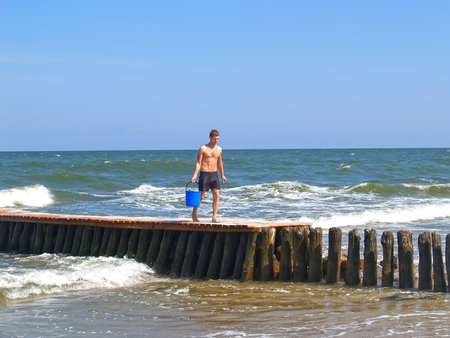 ZELENOGRADSK, RUSSIA - JULY 12, 2011: The young man goes on an old breakwater with a water bucketのeditorial素材