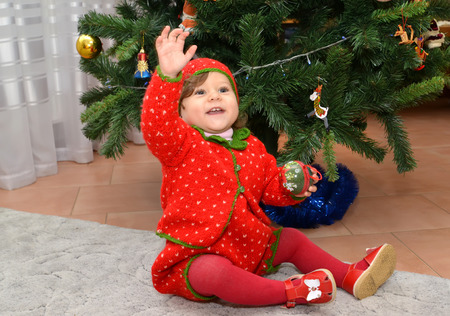 The little girl in the Strawberry suit with the raised hand sits about a New Year treeの写真素材