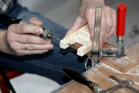 A man drills a hole in a wooden piece. Children 's master class on ship manufacturing