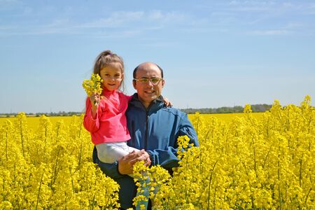 Man with daughter on hand standing in flowering rapeseed fieldの写真素材