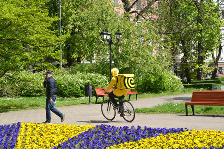 KALININGRAD, RUSSIA - MAY 07, 2020: Courier of fast food delivery service "Yandex Eda" rides a bicycle on a track in a square. Russian textのeditorial素材