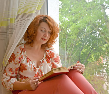 Portrait of a woman with a book in her hands sitting on a windowsill