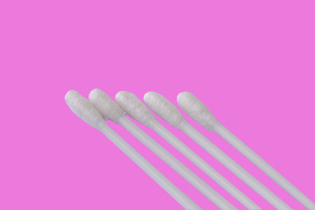 Five white cotton buds with plastic material isolated on a pink background, for the theme of health, beauty, and hygieneの写真素材
