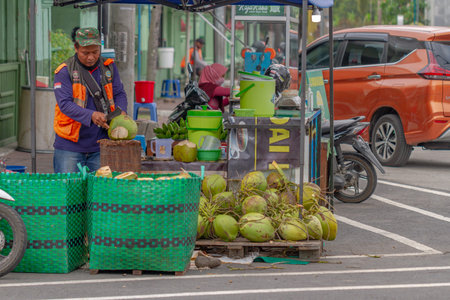 A young coconut seller without masker  is peeling coconuts on a hot day, in the area around Simpang...