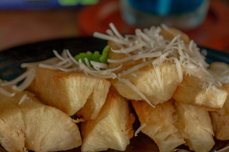 Fried Cassava with cheese sprinkles served on a black ceramic plate, a snack for lunch