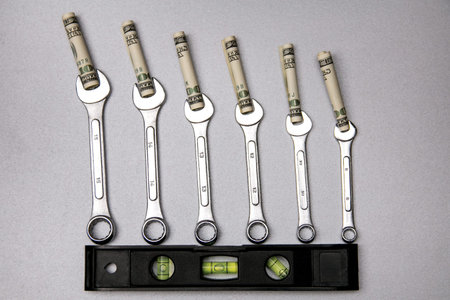 Concept of fixing currency of money and tools. Six wrenches, waterpass and dollars on gray