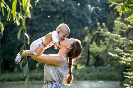 Happy mother with baby son standing in the park. Mother playing with little son at parkの写真素材
