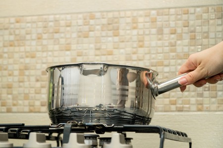 Womans hand holds big pot in modern kitchenの写真素材