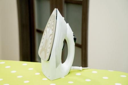 Modern electric iron on ironing board in roomの写真素材