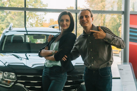 A woman and man in smart casual wear in auto show are standing a on car background