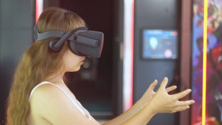 Girl wearing virtual reality glasses. Virtual reality installation on the backgroun. The girl holds a virtual object in her handsの写真素材