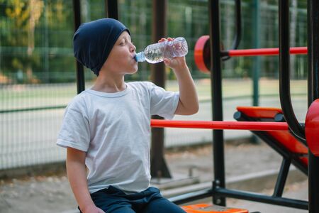 Little boy drinking water near outdoor public fitness equipmentの写真素材