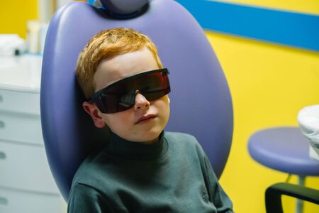 Scared red-haired boy crying at reception at dentist in dental chairの写真素材