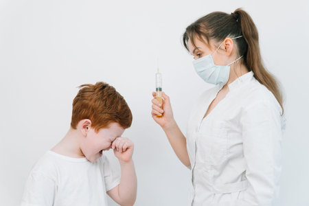 Little boy is afraid of the doctor with a syringe. Baby cries afraid injection. The doctor gives the...