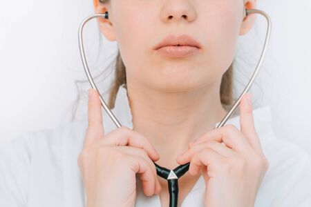 Portrait of a young woman doctor in a white coat with a stethoscope on a white background in a hospitalの写真素材