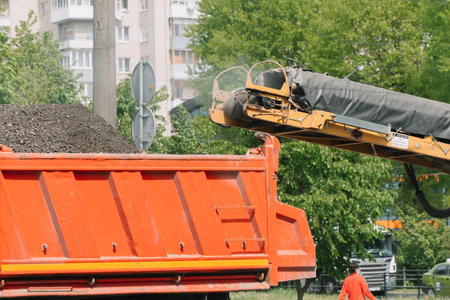 Dismantling of asphalt pavement. Workers cut off the old asphalt and poured it into the back of the...