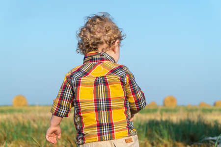 Little fair-haired boy playing on a wheat field with balesの写真素材