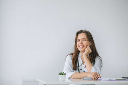 Smiling female physician posing while sitting at the table in hospital office. Medicine conceptの写真素材