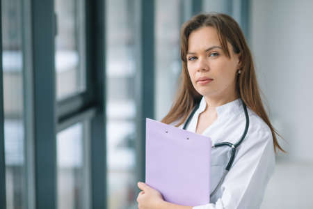Smiling female physician posing in hospital office near the windowの写真素材