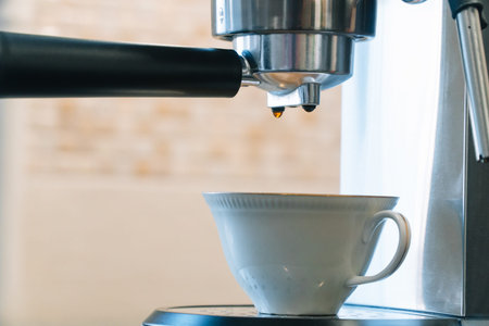 The process of pouring coffee from a coffee machine into a small white porcelain cup with gilding