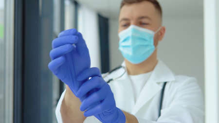 Young doctor in a protective mask puts on medical glovesの写真素材