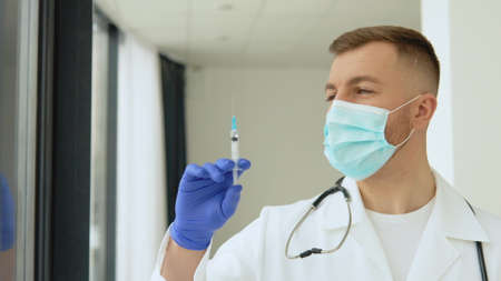 Young doctor in a protective mask with a vaccine syringe in his handsの写真素材
