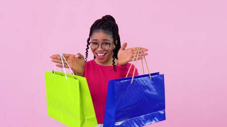 Young african american girl in pink clothes having fun and dancing with paper laminated bags with...