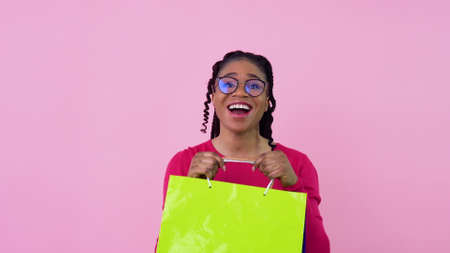 Young african american girl in pink clothes having fun and dancing with paper laminated bags with handles. Teen girl standing on a solid pink backgroundの写真素材