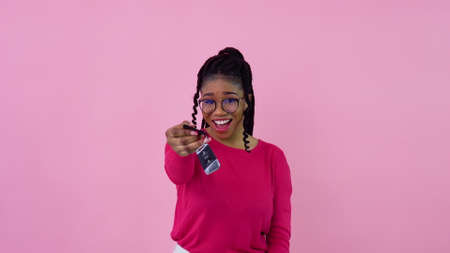 Cute cheerful young african american girl holding a car key. Teen girl housewife beginner standing on a solid pink backgroundの写真素材
