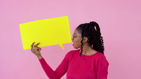 Cute young african american girl stands with posters for expression on a solid pink background. A place for advertising slogansの写真素材