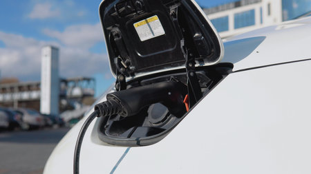 Electric car charging batteries with electricity through power cable on parking lot